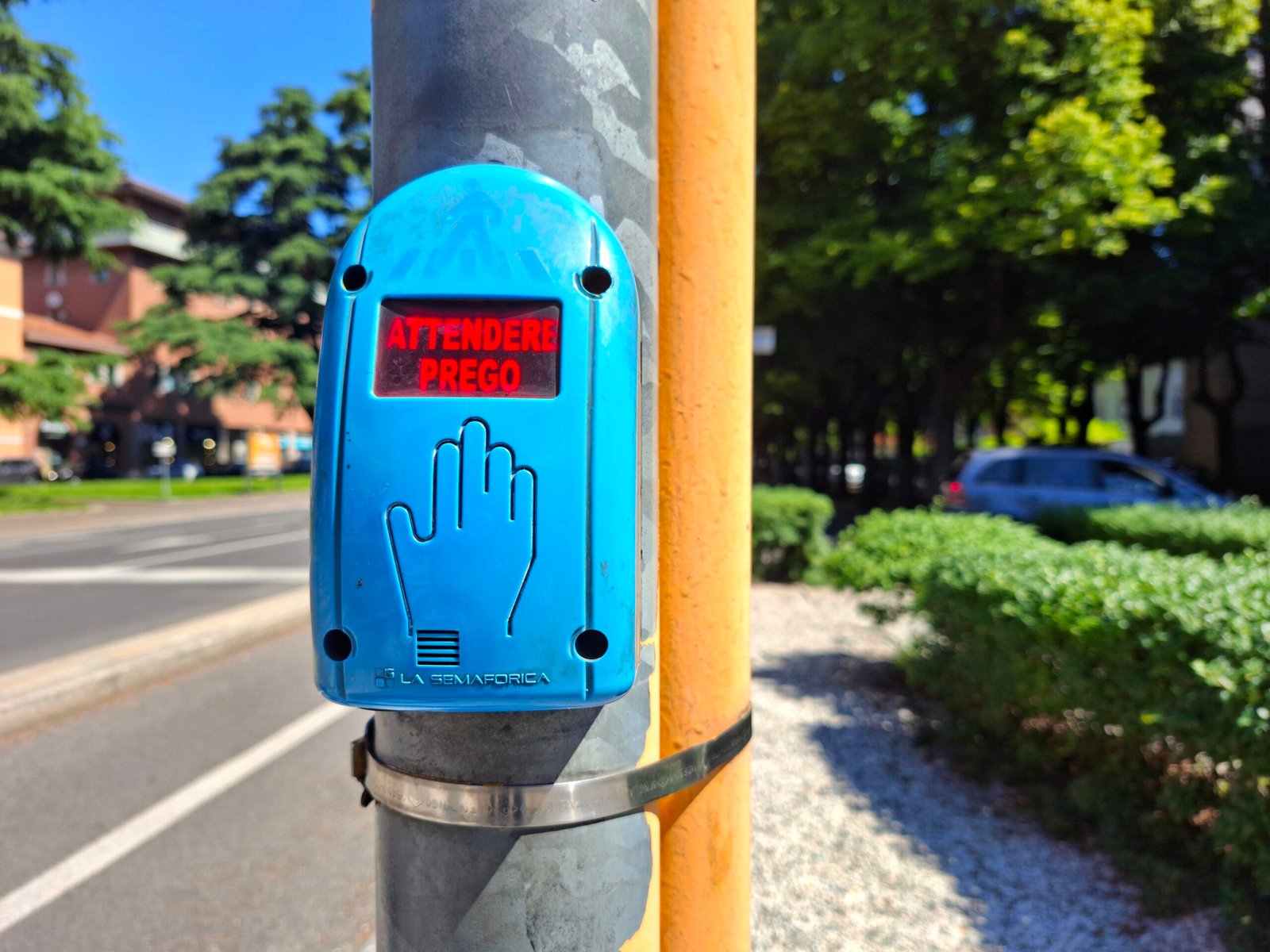 A pedestrian crossing button with the red Italian text "ATTENDERE PREGO" (Please wait)