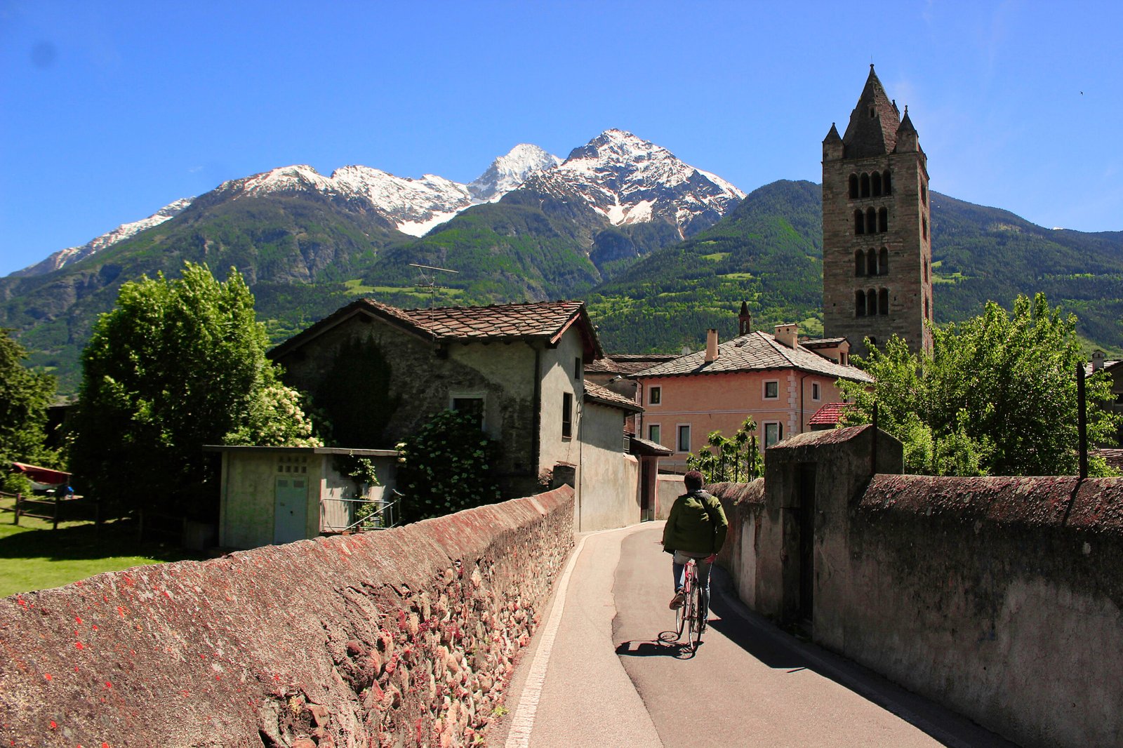 A citizen of the alpine city Aosta of Valle d'Aosta region, biking in a narrow alley in the historical town, 2024.